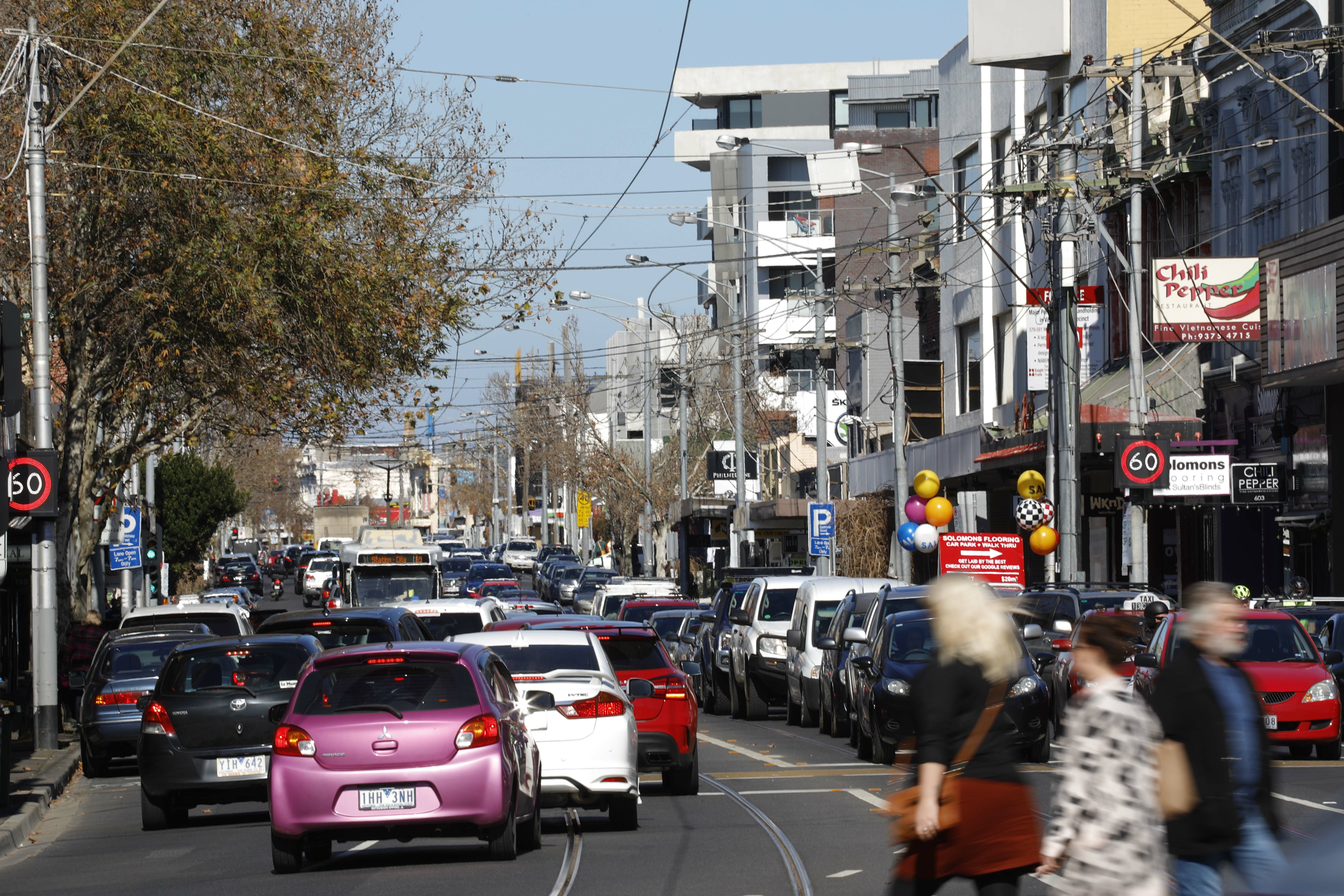 Ascot Vale street with cars, pedestrians, shops and apartments