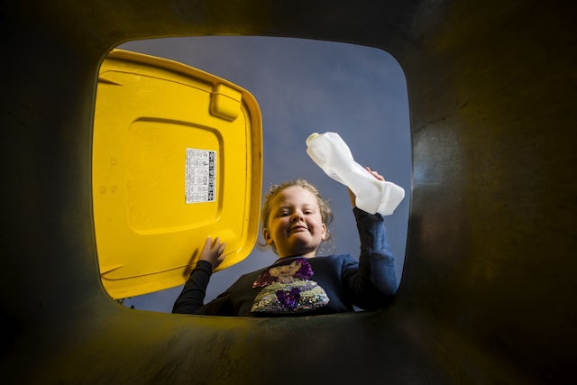 child putting recycling in yellow lidded bin