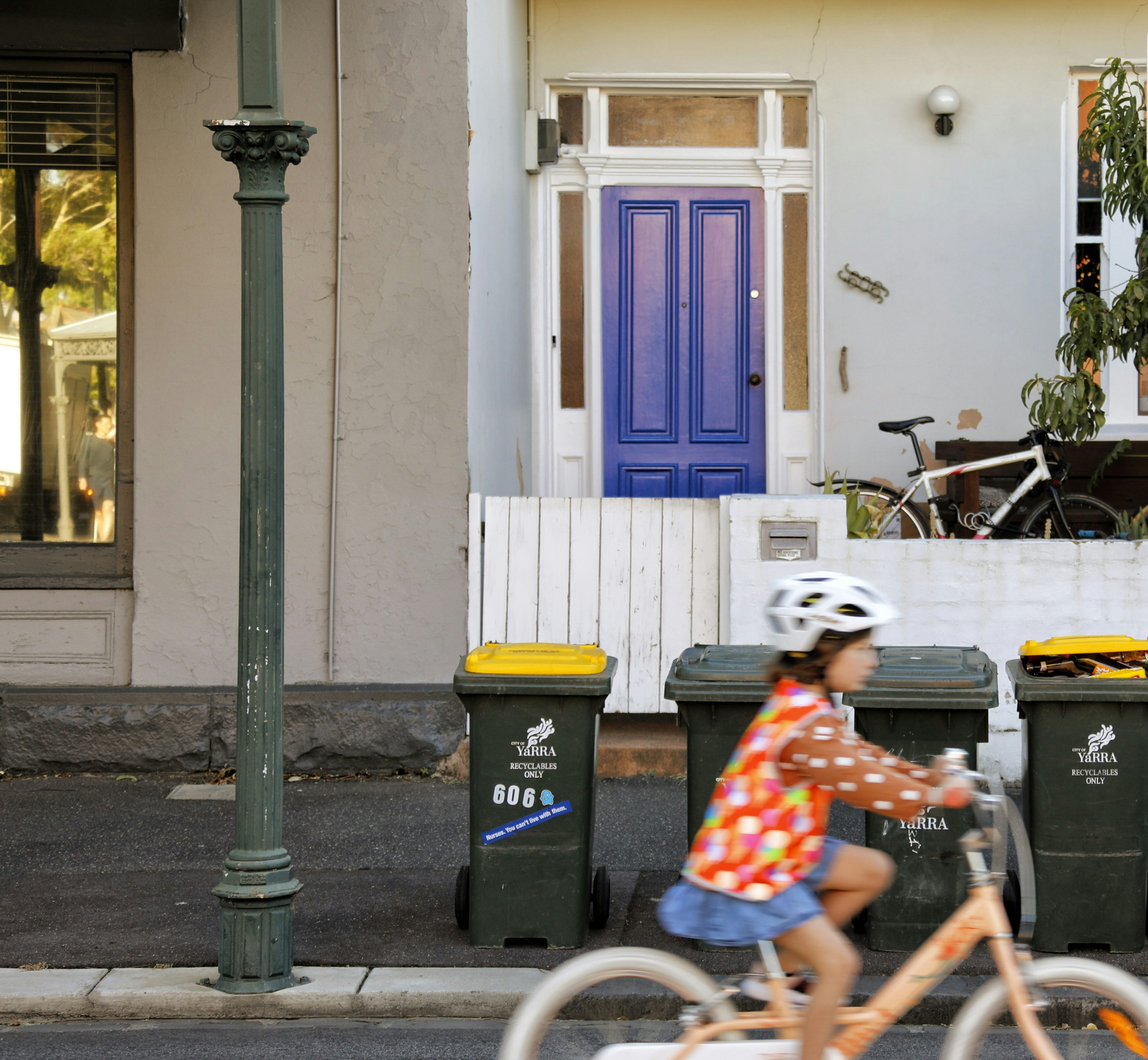 Young girl riding bike past kerbside bins